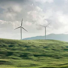 Wind turbines on rolling green hills under a cloudy sky, representing sustainable energy and optimized performance.